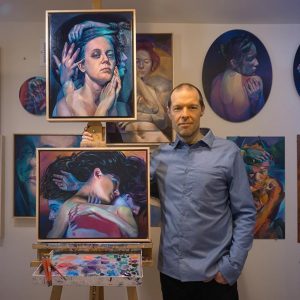 Scott Hutchison standing next to two of his paintings in his studio